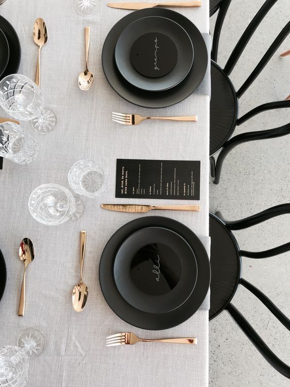 the table is set with black plates, silverware and gold utensils on it