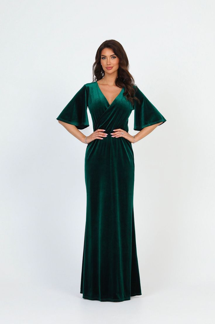 a woman wearing a green velvet gown with an open back and short sleeves, standing in front of a white background