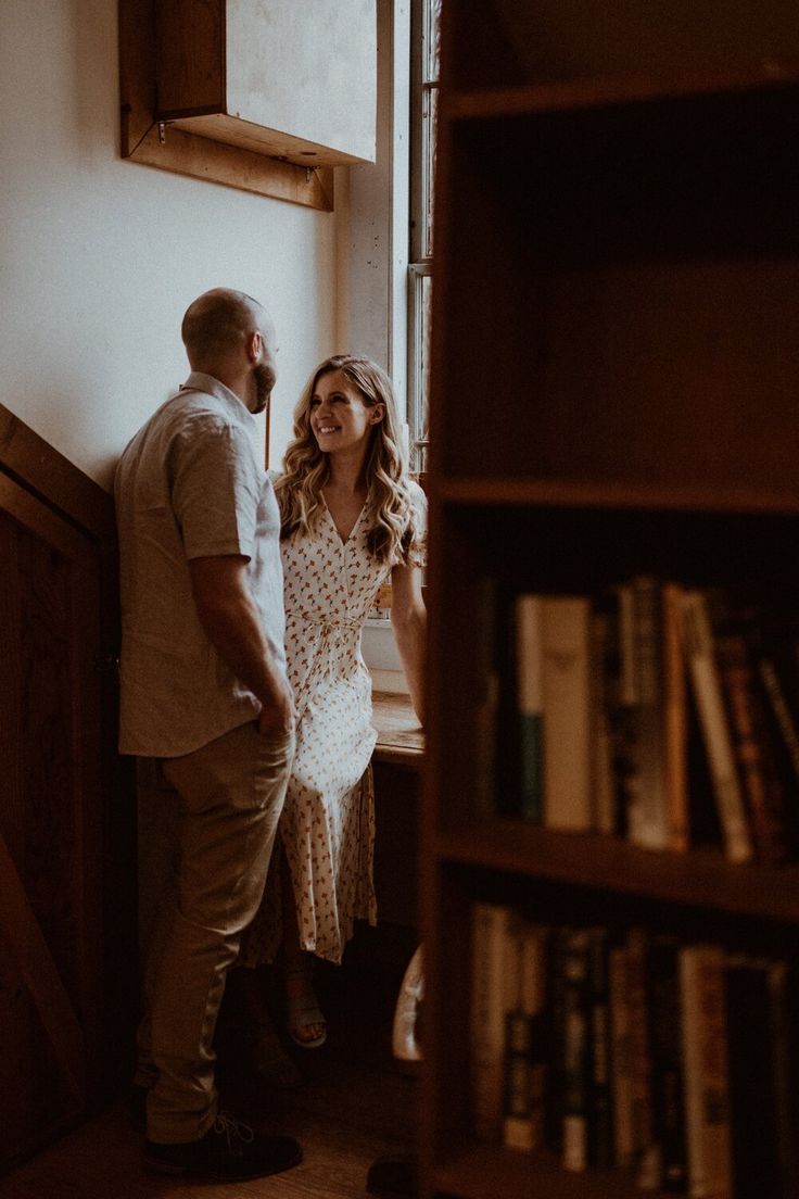 a man and woman standing next to each other in front of a book shelf filled with books