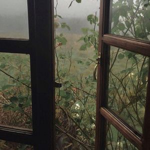 an open window looking out at a field and trees in the distance with fog on them