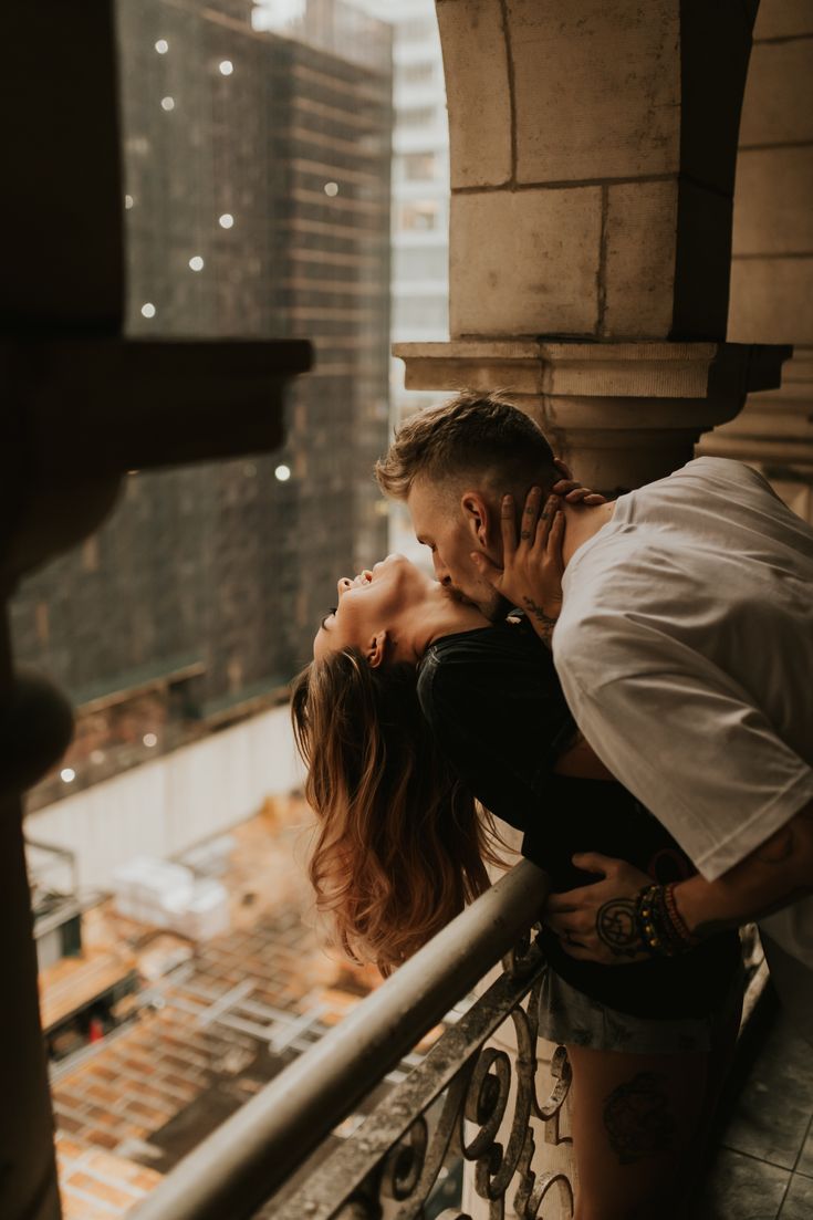 a man kissing a woman on the cheek while standing next to a railing with buildings in the background