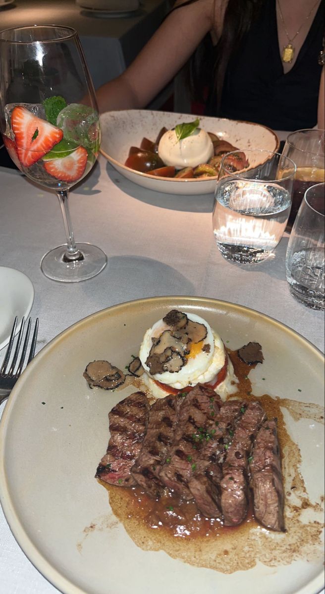 a steak dinner is served on a white plate at a table with wine glasses and utensils