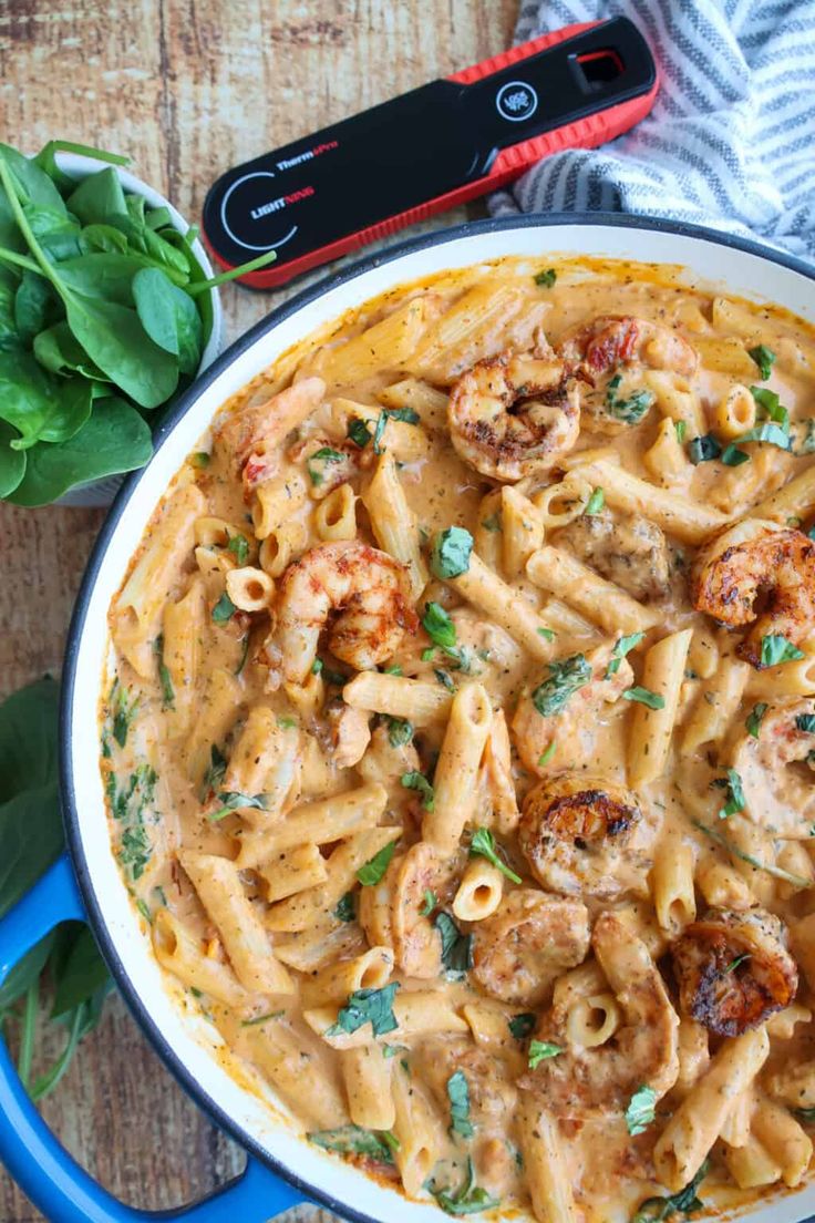 pasta with shrimp and sauce in a blue skillet on a wooden table next to basil