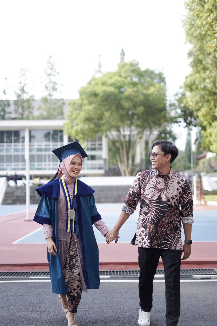 two people holding hands and walking down the street with their graduation gowns draped over them