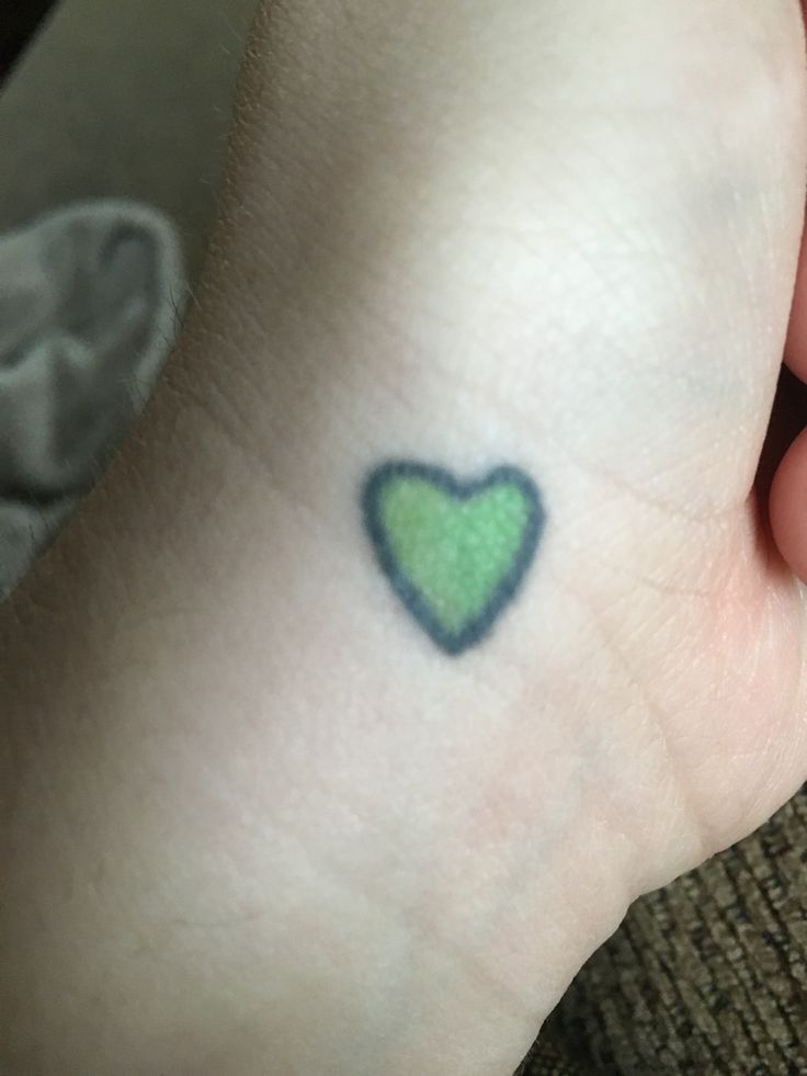 a small green heart tattoo on the left wrist and right hand, with blue ink