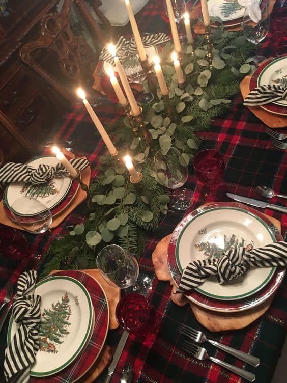 the table is set for christmas dinner with candles and plaid napkins on top of it