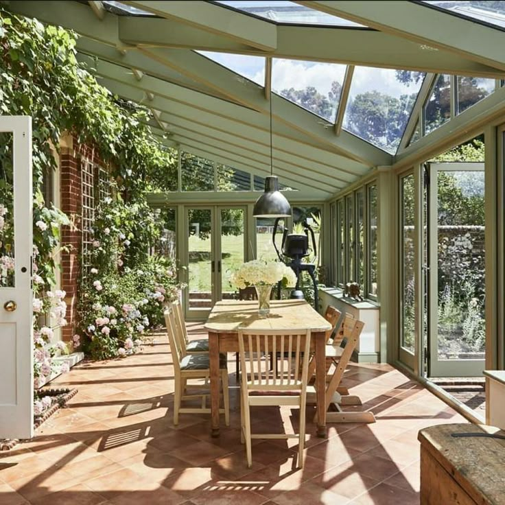 a table and chairs in a room with glass walls on both sides, surrounded by greenery