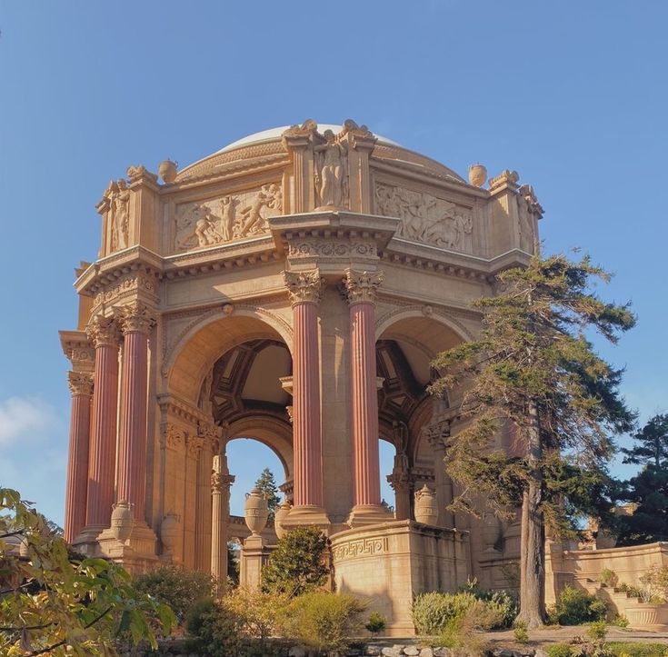 an ornate building with columns and statues on the top, surrounded by greenery under a blue sky