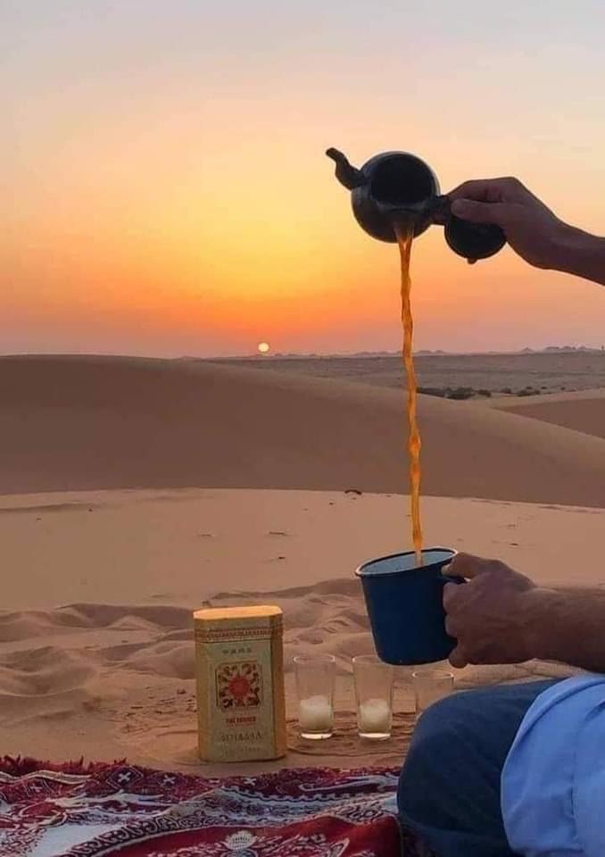 a man sitting on top of a blanket in the desert drinking from a blue cup