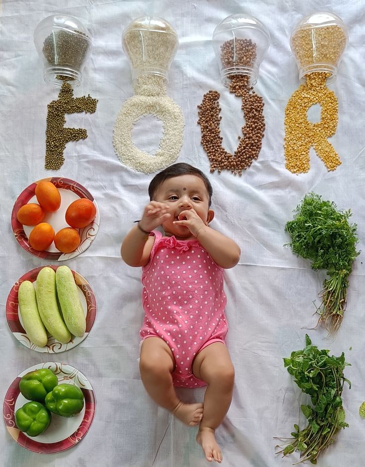 a baby is laying down in front of some vegetables and fruits on a table with the word food spelled out