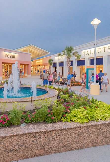 people are walking around in front of a store with fountains and flowers on the ground