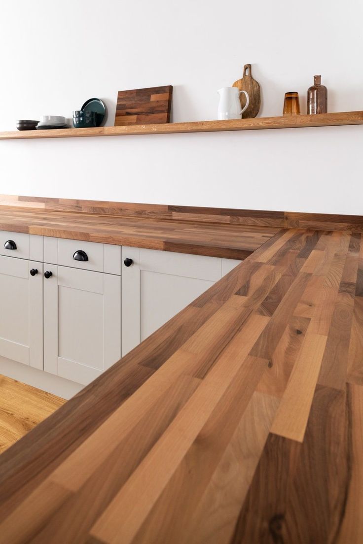 a wooden counter top in a kitchen with white cabinets and wood shelves on the wall