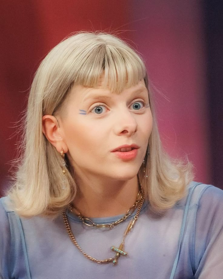 a close up of a person with a necklace on and an earring in front of her