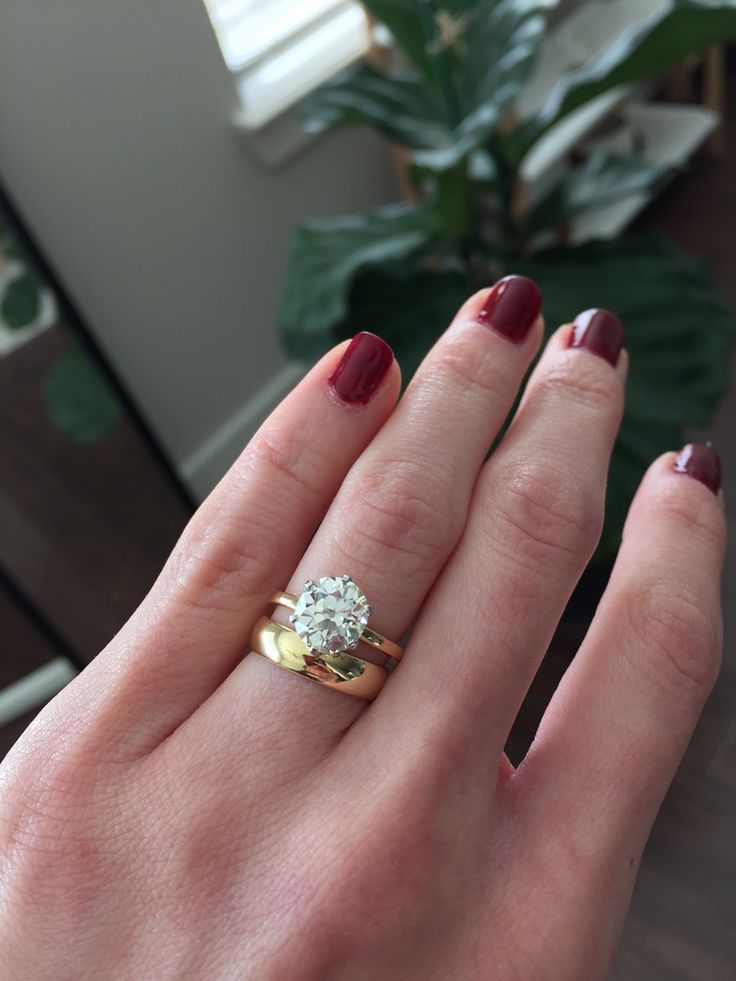 a woman's hand with a ring on it and a plant in the background