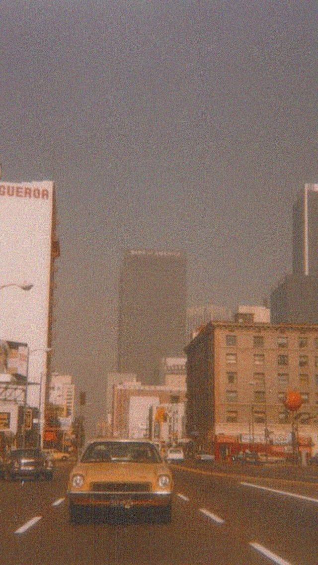 a yellow car is driving down the street in front of tall buildings and skyscrapers