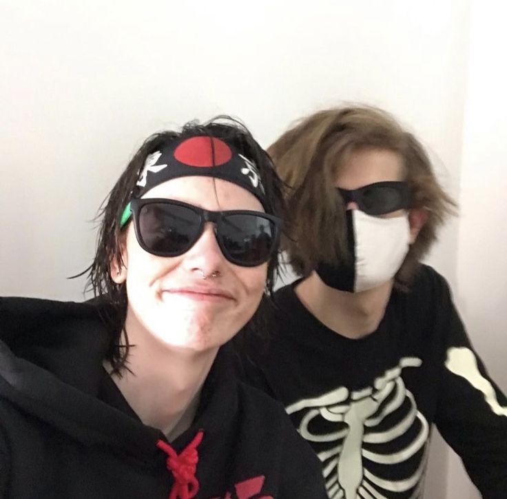 two people wearing face masks and skeleton shirts in front of a wall with white walls