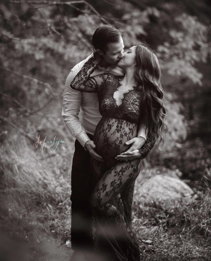 a pregnant couple kissing in the woods