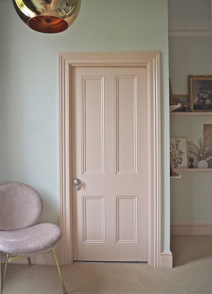 a pink chair sitting next to a white door in a room with a light fixture above it