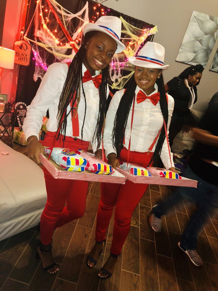 two women in red pants and white hats hold up birthday cakes while standing next to each other