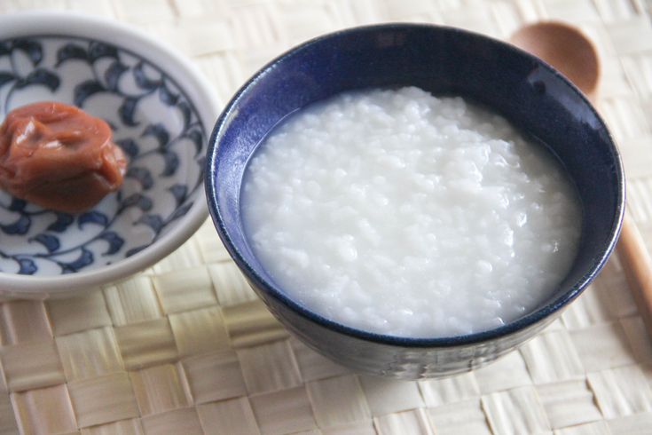 rice in a blue bowl next to a spoon on a woven place mat with a wooden spoon