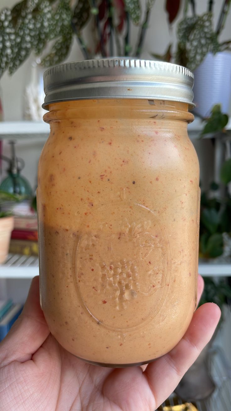 a hand holding a mason jar filled with peanut butter and sprinkled with cinnamon