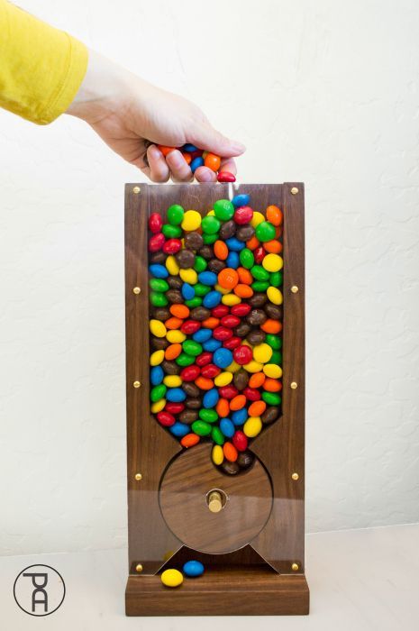 a person holding a wooden box filled with lots of colorful candies in front of a white wall