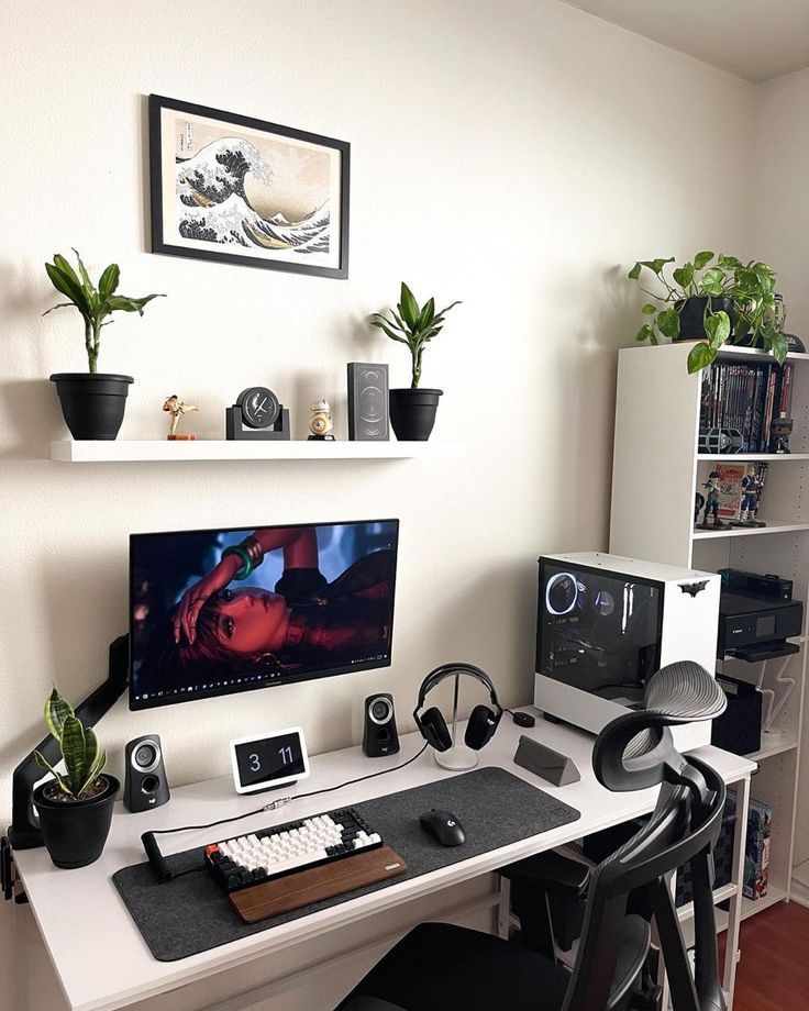 a desk with a computer monitor, keyboard and headphones on it in front of some plants