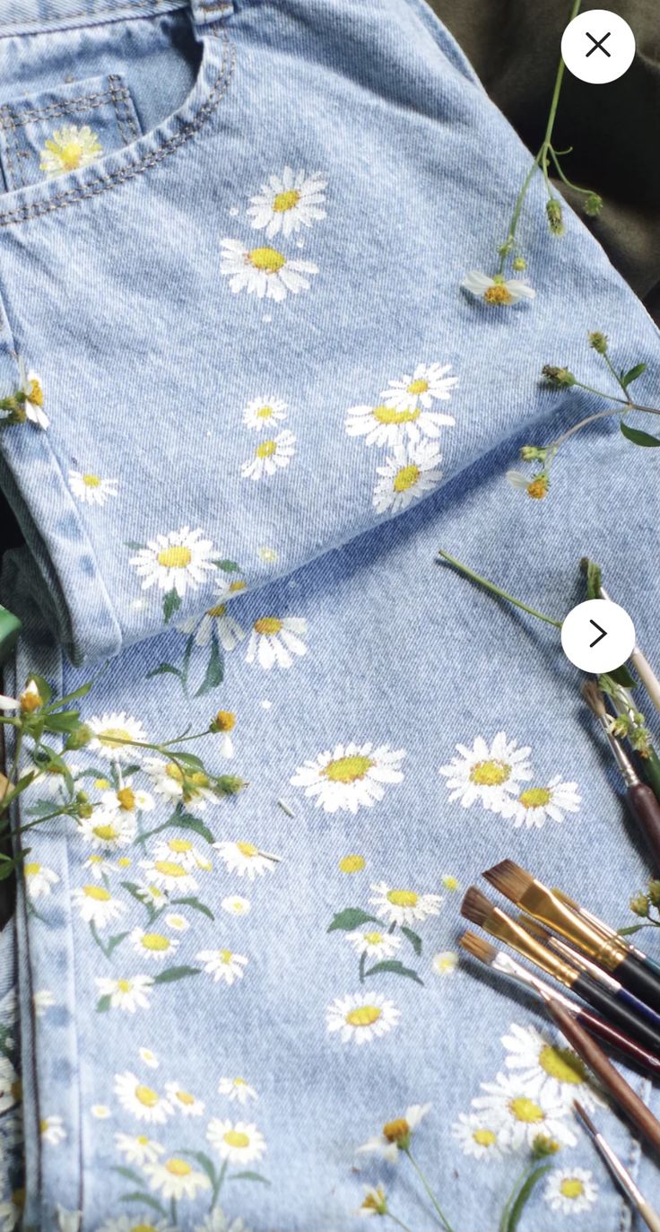 some paintbrushes are laying next to an old pair of jeans with daisies on them