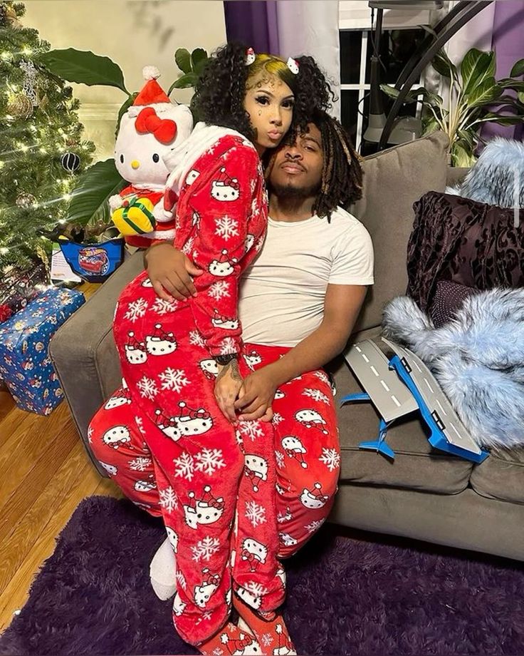 a man and woman sitting on a couch in matching christmas pajamas with hello kitty dolls