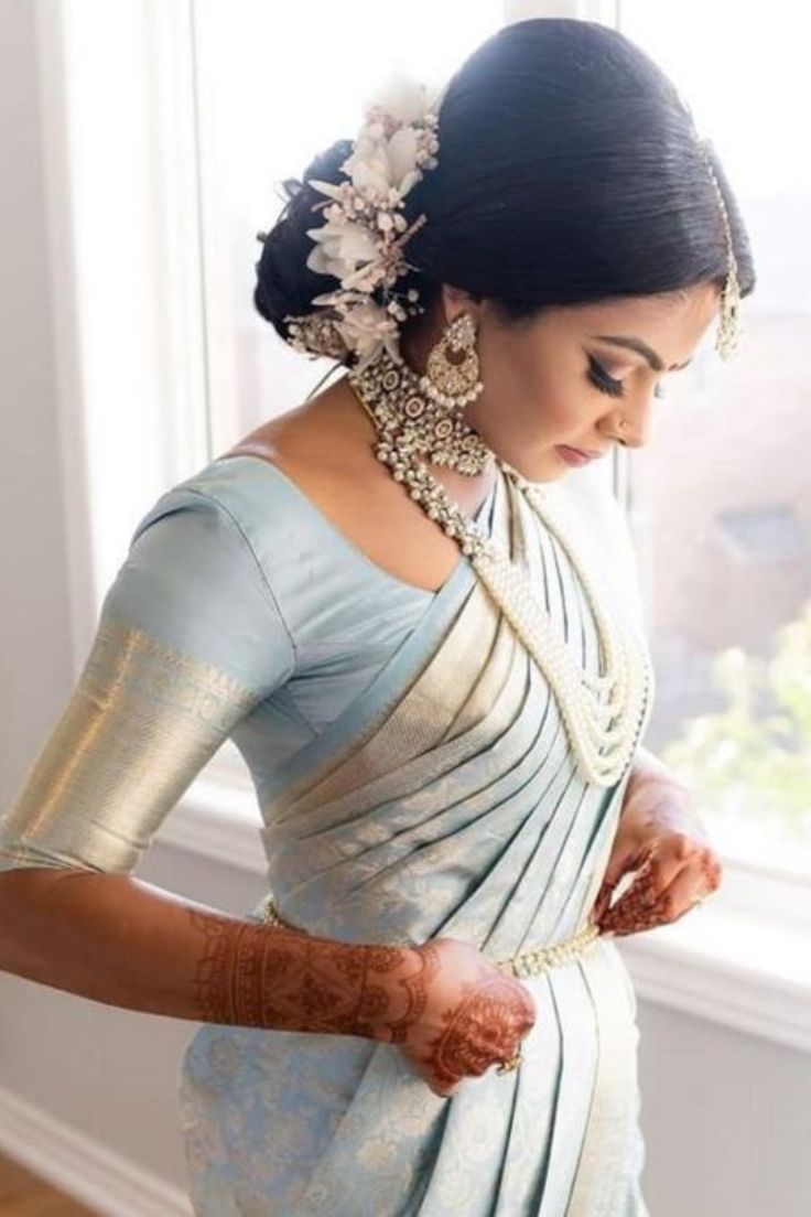 a woman in a white and blue sari is holding her hands together while looking out the window