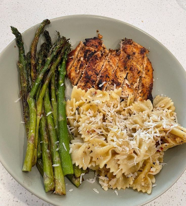 a white plate topped with meat, pasta and asparagus