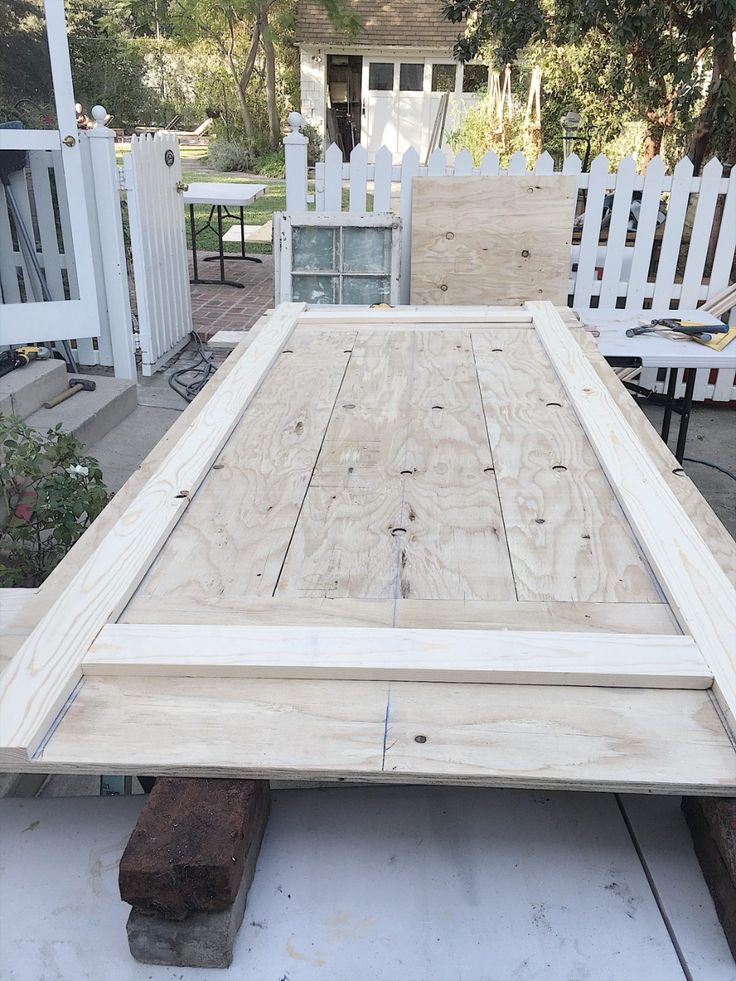 an unfinished bed frame sitting on top of a cement slab in front of a white picket fence