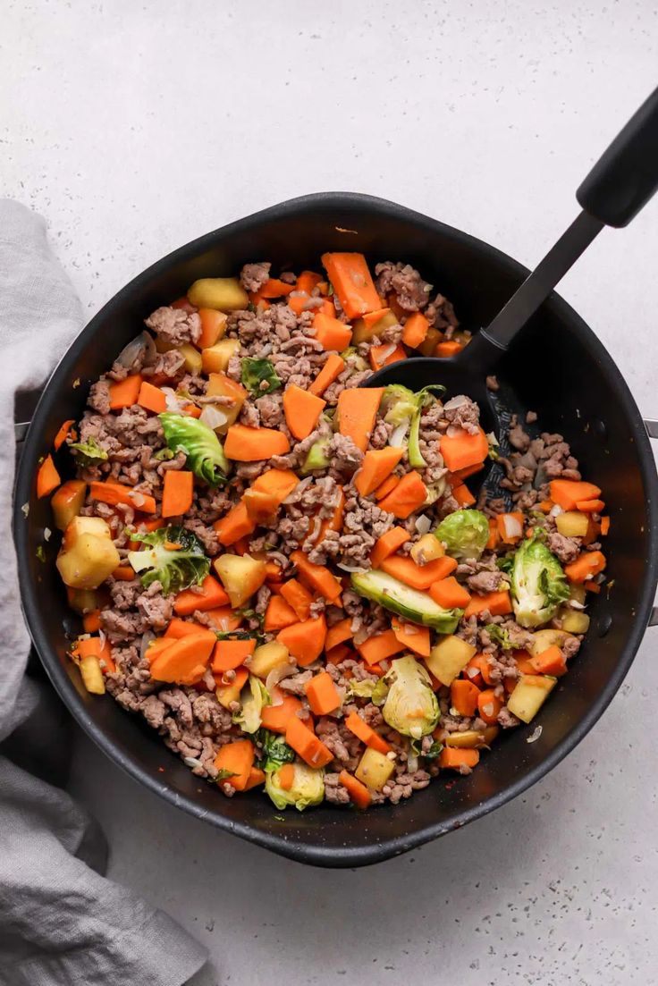 a skillet filled with meat and vegetables on top of a white tablecloth next to a napkin