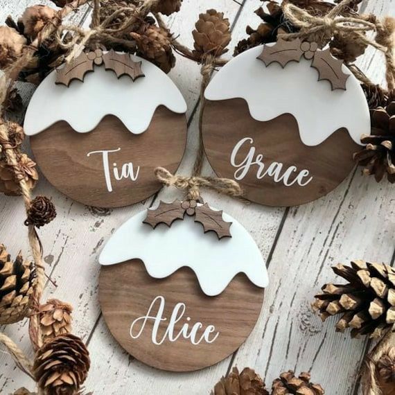 four wooden ornaments with white and brown designs on them, sitting next to pine cones