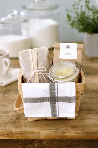 a basket filled with tea towels and soap on top of a wooden table next to a cup