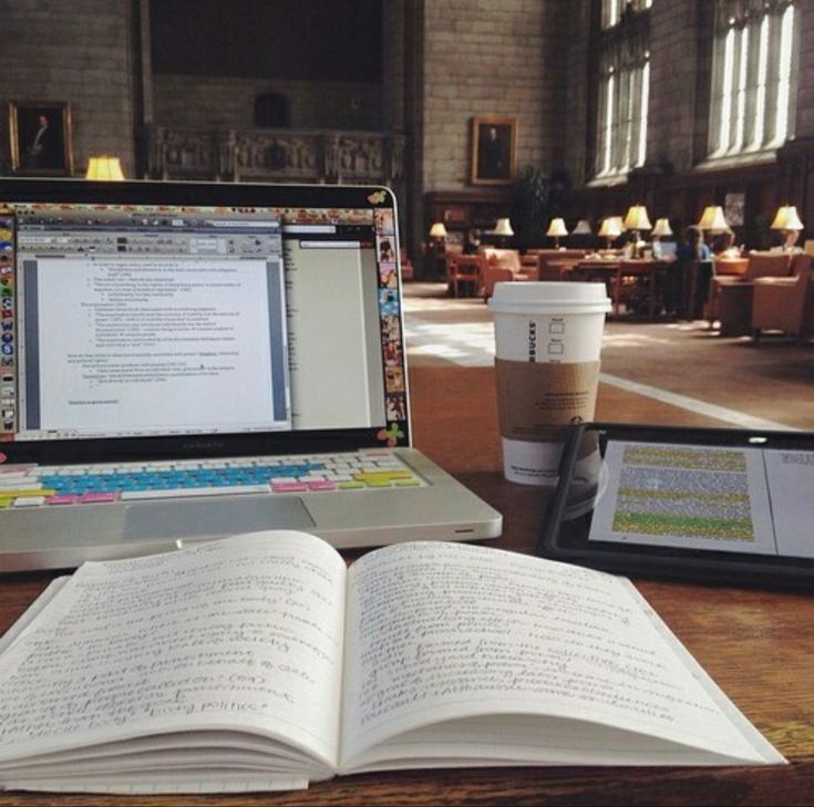 an open book sitting on top of a wooden table next to a laptop computer and tablet