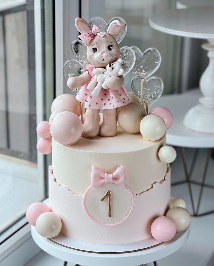 a pink and white cake with a bunny on top sitting in front of a window