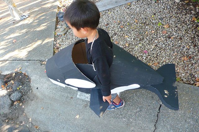 a young boy sitting on top of a fake shark shaped cardboard boat in the street