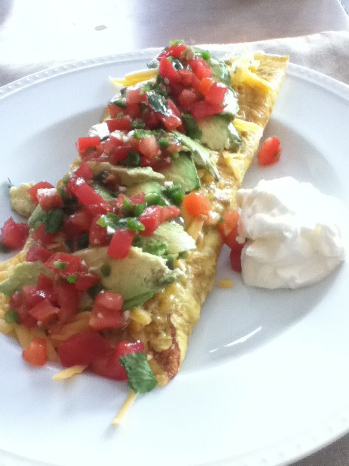 an omelet with tomatoes, avocado and sour cream on a plate