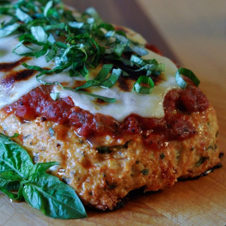 a piece of meat covered in sauce, cheese and greens on top of a wooden cutting board