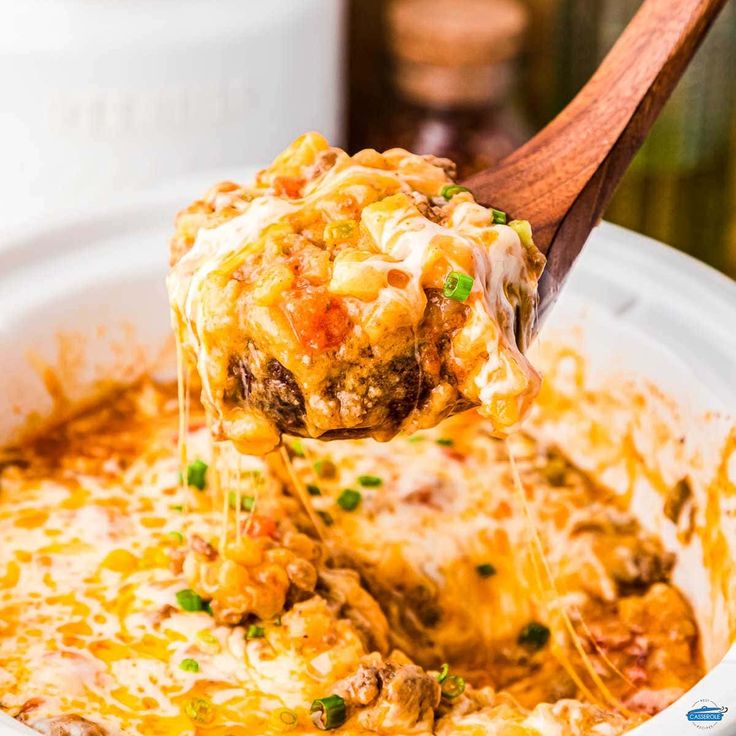 a wooden spoon full of cheesy lasagna casserole being lifted from a crock pot