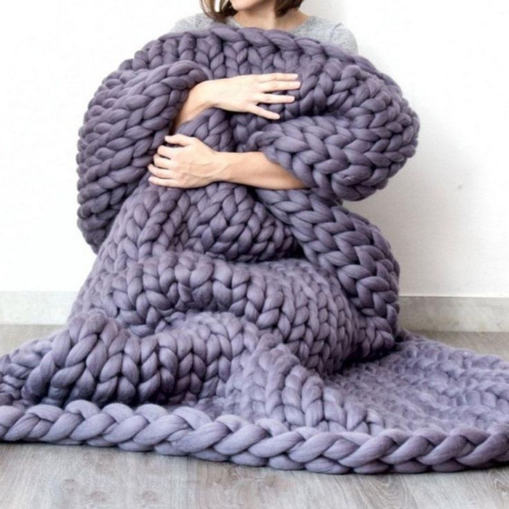 a woman wrapped in a giant chunky blanket with her hands on the back of it