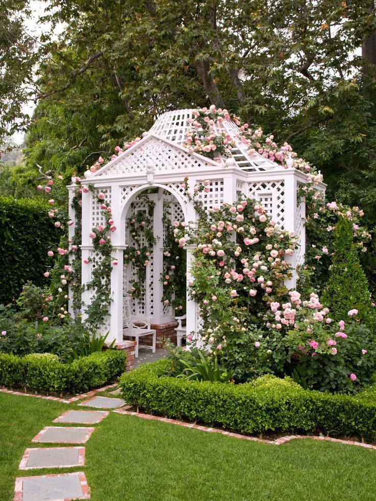 a white gazebo surrounded by lush green grass and pink roses in the garden area