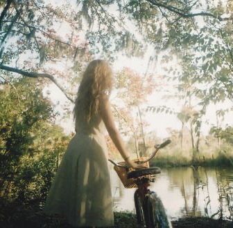 a woman in a dress standing next to a bike by the water's edge