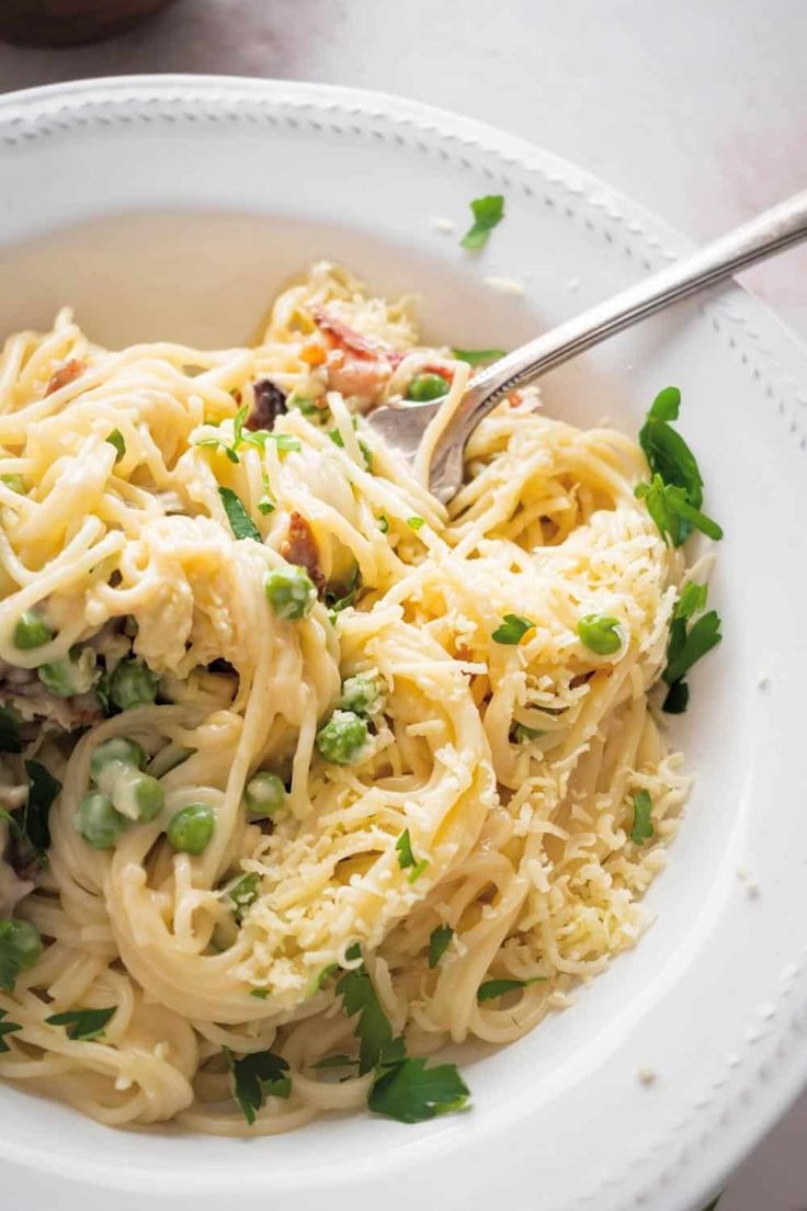 a white bowl filled with pasta and vegetables on top of a table next to a fork