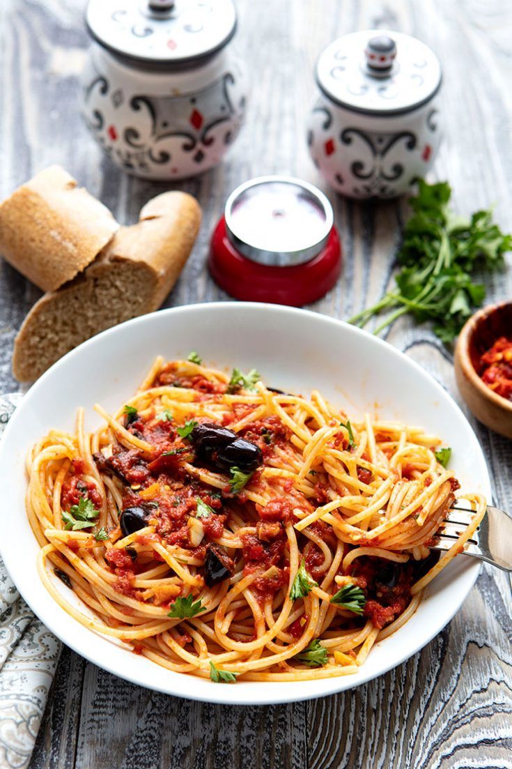 a white bowl filled with pasta and sauce next to bread on a wooden table top