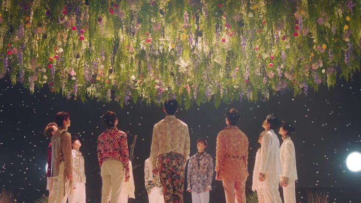 the models are all dressed up in white and floral outfits, standing under a flower - filled chandelier