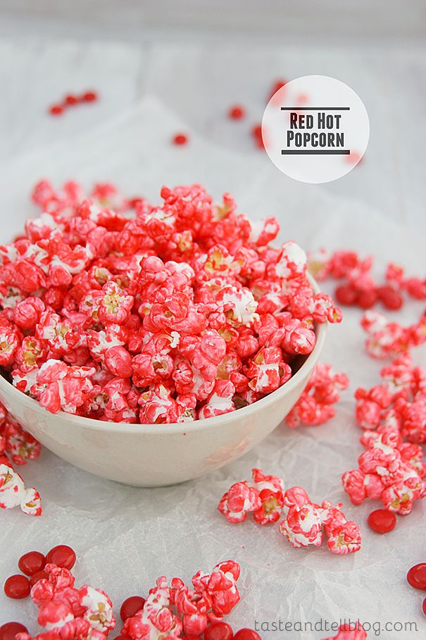 a bowl full of red and white popcorn sitting on top of a table next to candy