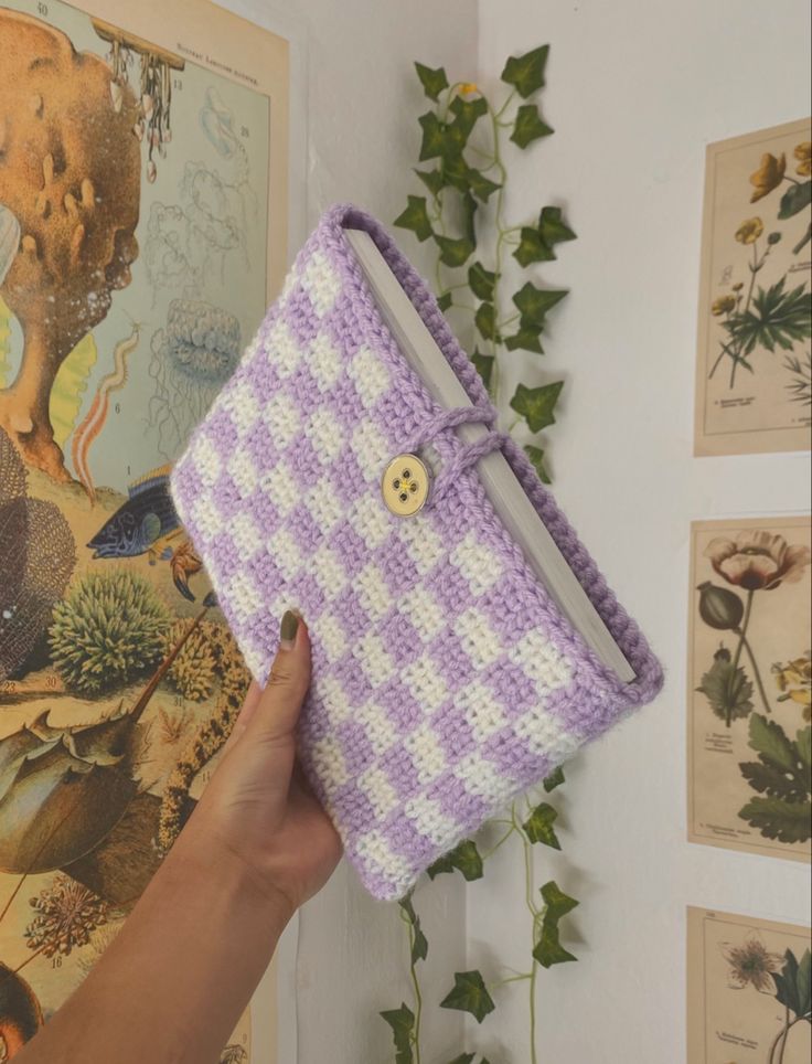 a hand is holding a crocheted purple and white purse with a button on it