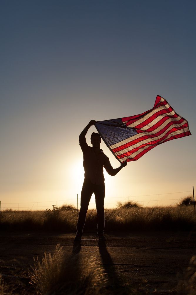 a man holding an american flag in front of the sun with a quote on it